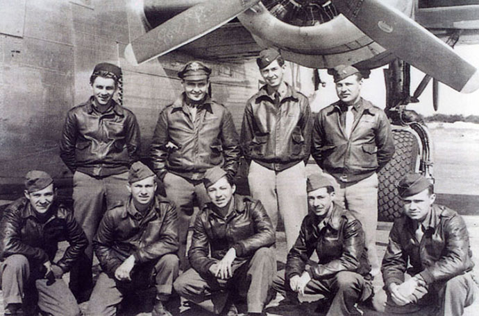 Nine members of a B-24 bomber crew in uniform posing in front of aircraft