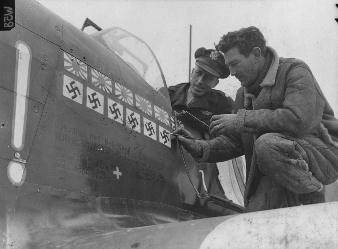 Major James H Howard of the 354th Fighter Group watches Staff-Sergeant Marcus Hanson paint a "kill" onto his new P-51 Mustang. Image stamped on reverse: 'Associated Press.' [stamp], 'Passed for publication 25 Jan 1944.' [stamp] and '301687.' [Censor no.] Printed caption on reverse: 'NEW SHIP FOR MAJOR HOWARD. American Fighter Ace Major James H Howard of St Louis, MO, has now taken over a new ship- one of the crack P-51Bs which have been making aerial history recently. Major Howard has the following decora