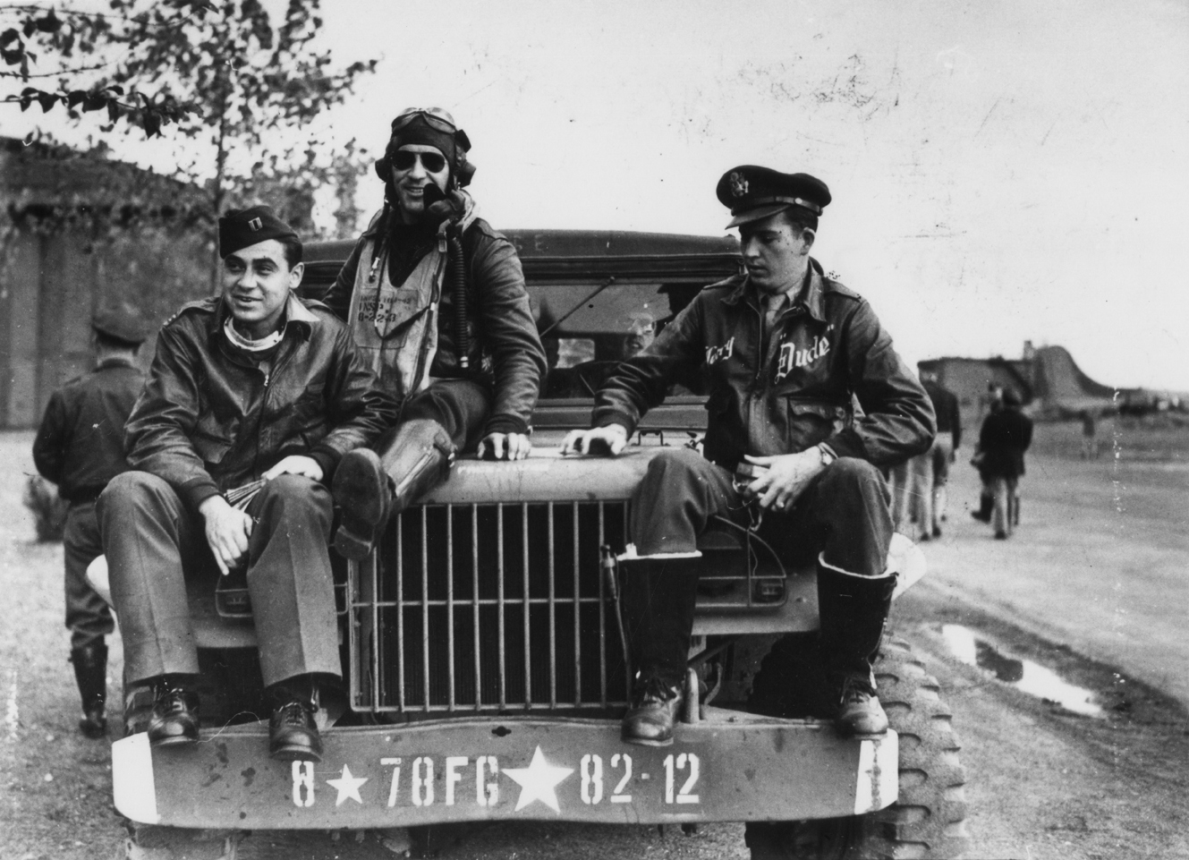 From left to right: Captain Walker L. Boone, Flight Officer Manuel S. Martinez and Flight Officer Gerry E. Brasher, pilots of the 82nd Fighter Squadron, 78th Fighter Group, sit on the bonnet of a jeep at Duxford air base. Passed for publication 28 October 1943. Printed caption on reverse: 'Thunderbolts - the "Guardian Angels" of Flying Fortresses. Here are pictures of Thunderbolts P-47s, the famous American fighter planes, which escort Flying Fortresses on their daylight missions over Occupied Europe. Pho