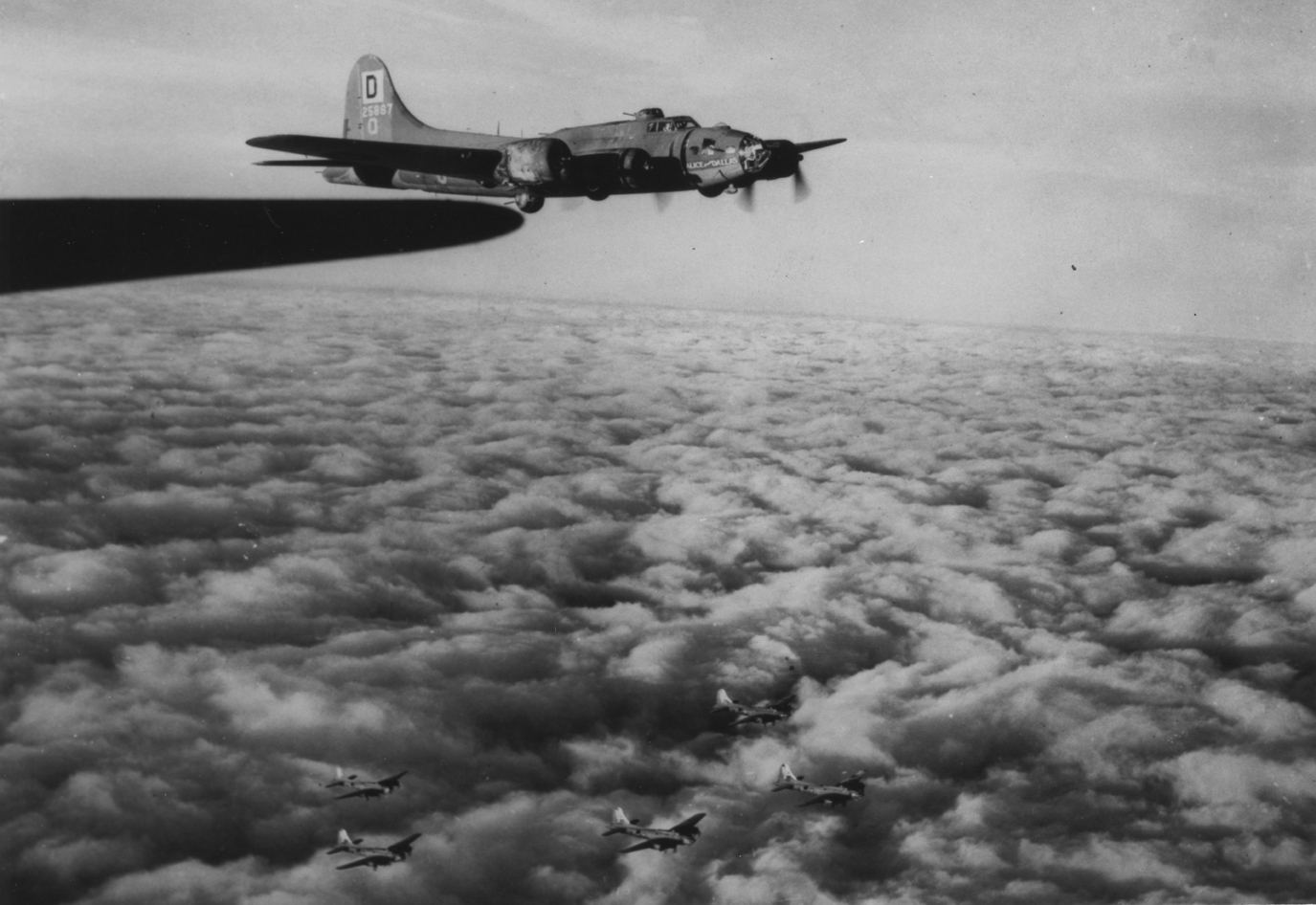 A B-17 Flying Fortress (**-O, serial number 42-5867) nicknamed "Alice from Dallas" of the 100th Bomb Group flies in formation above the clouds with other Fortresses. Printed caption on reverse: 'A formation of B-17 "Flying-Fortresses" of the 100th Bomb Group flyes[sic] over a blanket of clouds en route to their target at Warnemunde, Germany. The plane in the foreground is the B-17 "Alice From Dallas". 29 July 1943. US Air Force Photo.' Handwritten caption on reverse: '100BG.'