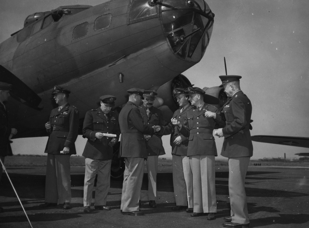 United States Air Chiefs of the European Theatre of Operations stand with a B-17 Flying Fortress of the 97th Bomb Group. Left to right these are: Major-General Frank, Brigadier-General Ira Eaker, Brigadier-General Robert Candee, Brigadier-General Frank O'Driscoll Hunter, Major-General Karl Spaatz and Lieutenant-General Dwight D. Eisenhower. Image stamped on reverse: 'Associated Press.' [stamp], 'Passed for Publication 2 Aug 1942.' [stamp] 'USA (BRI) CCC: STF.' [written annotation] and '213540.' [Censor no