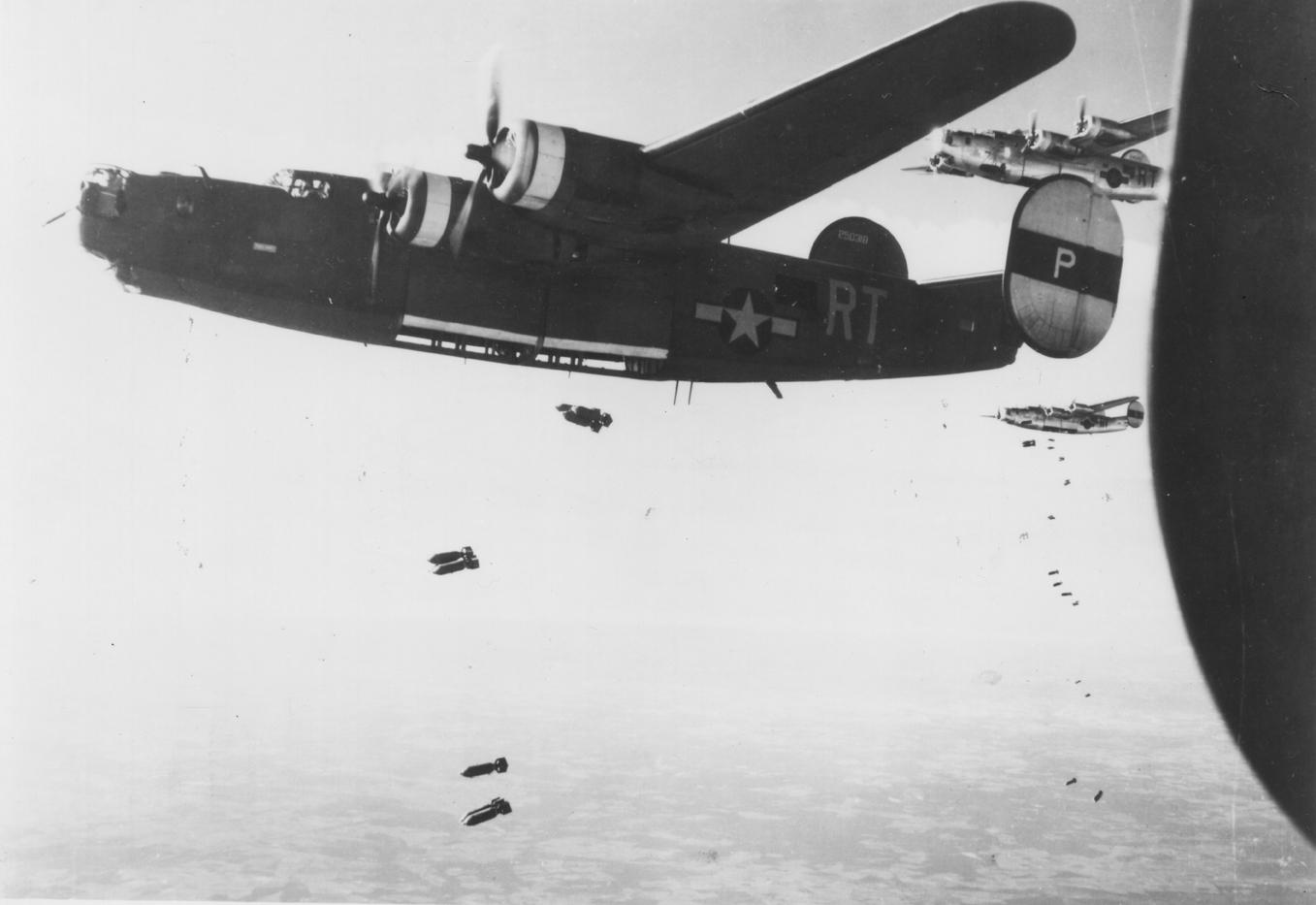 A B-24 Liberator (serial number 42-50318) of the 446th Bomb Group drops its load over the target area in Orleans, France during a mission with fellow Liberators. Printed caption on reverse: '81185 AC- Consolidated B-24's drop tons of bombs on the Nazi airdrome at Orleans, France during a raid on 14 June 1944.'