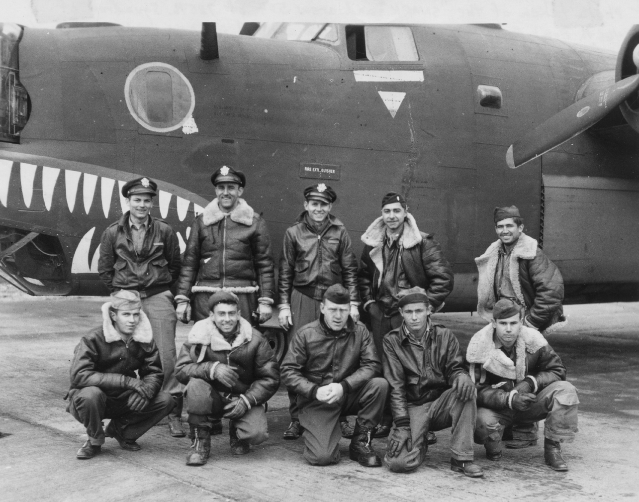 A bomber crew of the 466th Bomb Group with their shark mouth B-24 Liberator (serial number 41-29387) nicknamed "The Snafu Snark". First handwritten caption on reverse: 'Photo taken of the "SNARK" and crew 504 of 785th Squadron of the 466th Bomb Group, Eighth Air Force, on arrival at Attlebridge, England on Feb 25 1944. Top Row (left to right) Malcolm O Dike, Pilot, Claude V Meconis, co-pilot, William L Brooks, Navigator, Harold K Miller, bombardier, Julian R Thomspn, engineer. Bottom row (left to right) J