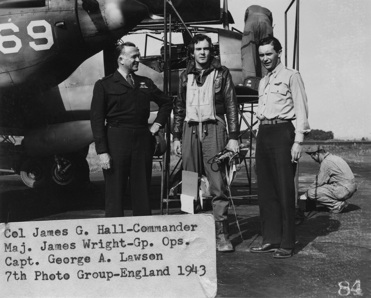 Colonel James G Hall, Commander, Major James Wright, Group operations and Captain George A Lawson of the 7th Photographic Reconnaissance Group with the nose of an F-5 Lightning. 1943. Image stamped on reverse: 'Passed by AAF STA 234. Not to be published.' [stamp]