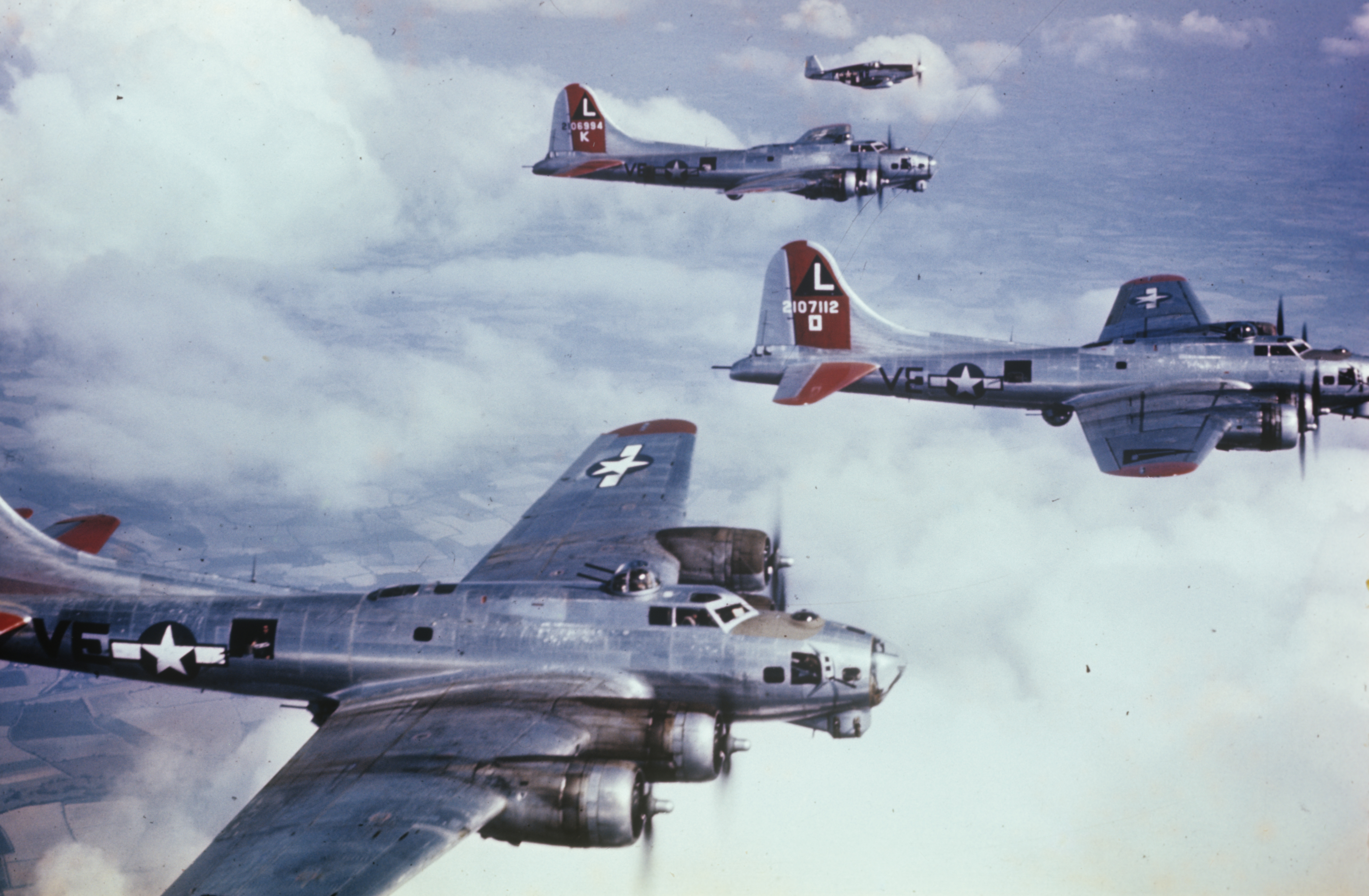 B-17 Flying Fortresses of the 381st Bomb Group are escorted during a practice mission by a P-51 Mustang of the 355th Fighter Group. The Fortresses, left to right, are (VE-N, serial number 43-37675) nicknamed "Patches (Flak Magnet)", (VE-K, serial number 42-106994) nicknamed "Little Guy" and (VE-O, serial number 42-107112) nicknamed "Sleepy Time Gal".