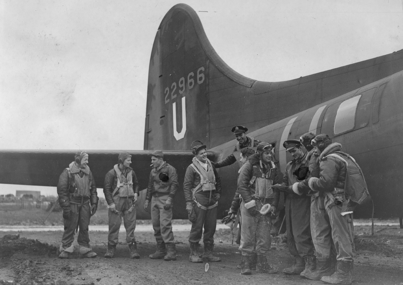 A bomber crew of the 303rd Bomb Group with their B-17 Flying Fortress. A censor has obscured the insignia on the men's jackets. Passed as censored 29 Jan 1943. Printed caption on reverse: 'First American Raid On Germany. Flying Fortresses And Liberators Of The U.S. Army Air Corps Carried Out Their First Raid On Germany On Wednesday Last. O.P.S., Left To Right: Sergt. Ward W. Kirkpatrick, (Kalispele, Mont.); T/Sgt. Lucian W. Means, (Luguna Beach, Cal.); 1st Lt. Milton K. Conver, (Cincinnatti, Ohio); 2nd Lt