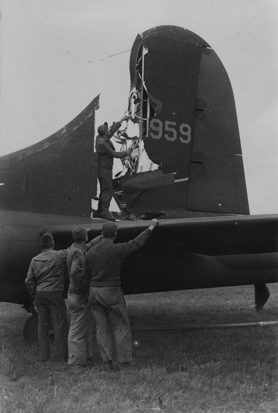 Ground crew of the 306th Bomb Group inspect the damaged tail of a B-17 Flying Fortress. Passed for publication 15 Jul 1943. Handwritten caption on reverse: '17/7/43.' Printed caption on reverse: 'Fortress Comes Home With Tail Almost Severed. After a recent raid on enemy territory, a Flying Fortress bomber managed to limp home with its tail almost severed. Photo Shows:- Inspecting the damaged Fortress bomber on its home airfield after its return.' On reverse: Planet News Ltd, US Army Press Censor ETO and U