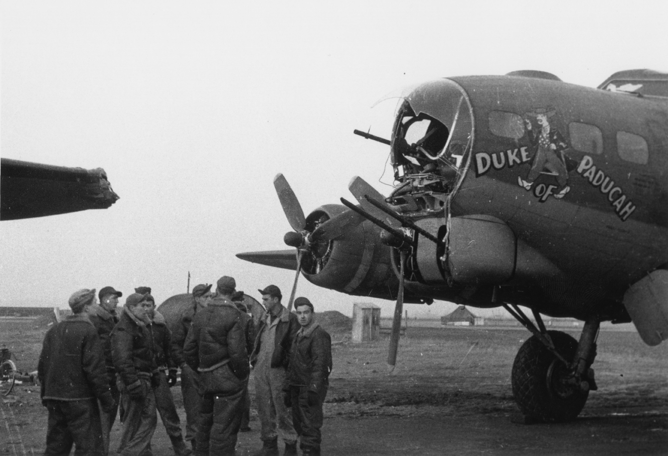 Personnel of the 91st Bomb Group gather by the battle damaged nose of a B-17 Flying Fortress nicknamed "The Duke of Paducah".