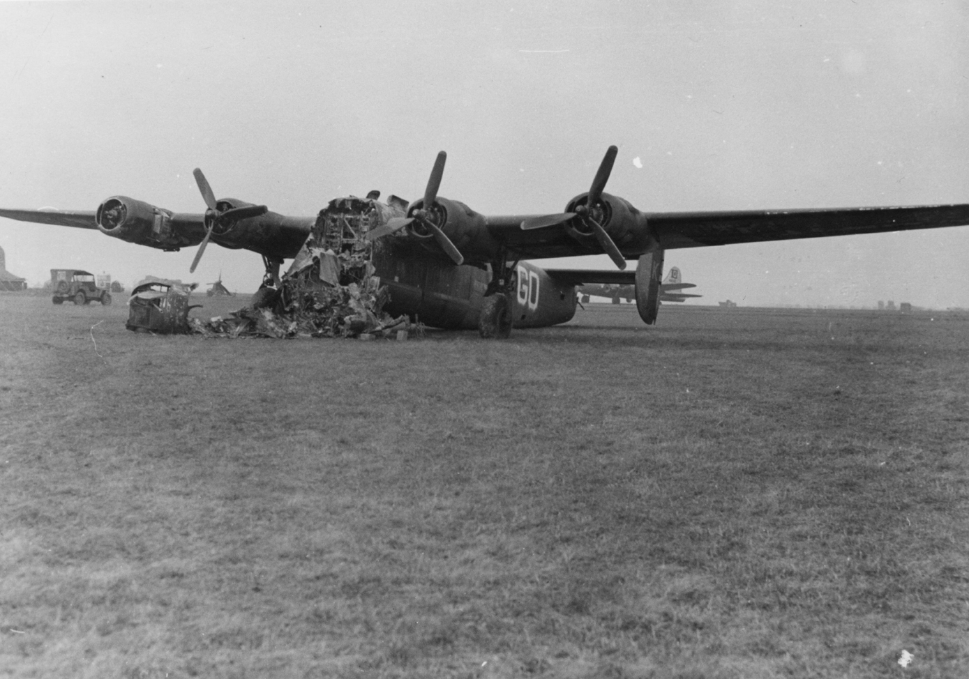 The wreckage of a B-24 Liberator (GO-K) of the 328th Bomb Squadron, 93rd Bomb Group that has crash landed. A B-17 Flying Fortress of the 100th Bomb Group is in the background.