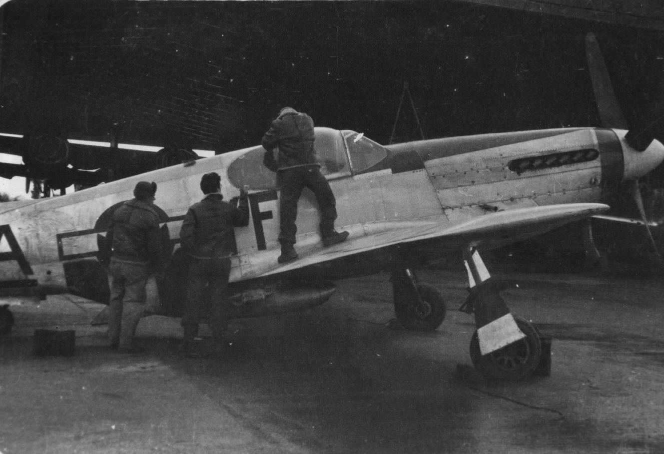 Personnel of the 358th Fighter Squadron, 355th Fighter Group examine a P-51 Mustang (YF-A_). A B-24 Liberator is in the background. Handwritten caption on reverse: 'YF-A_. Nose band colour? 358th FS, 355th FG. Hethel?'