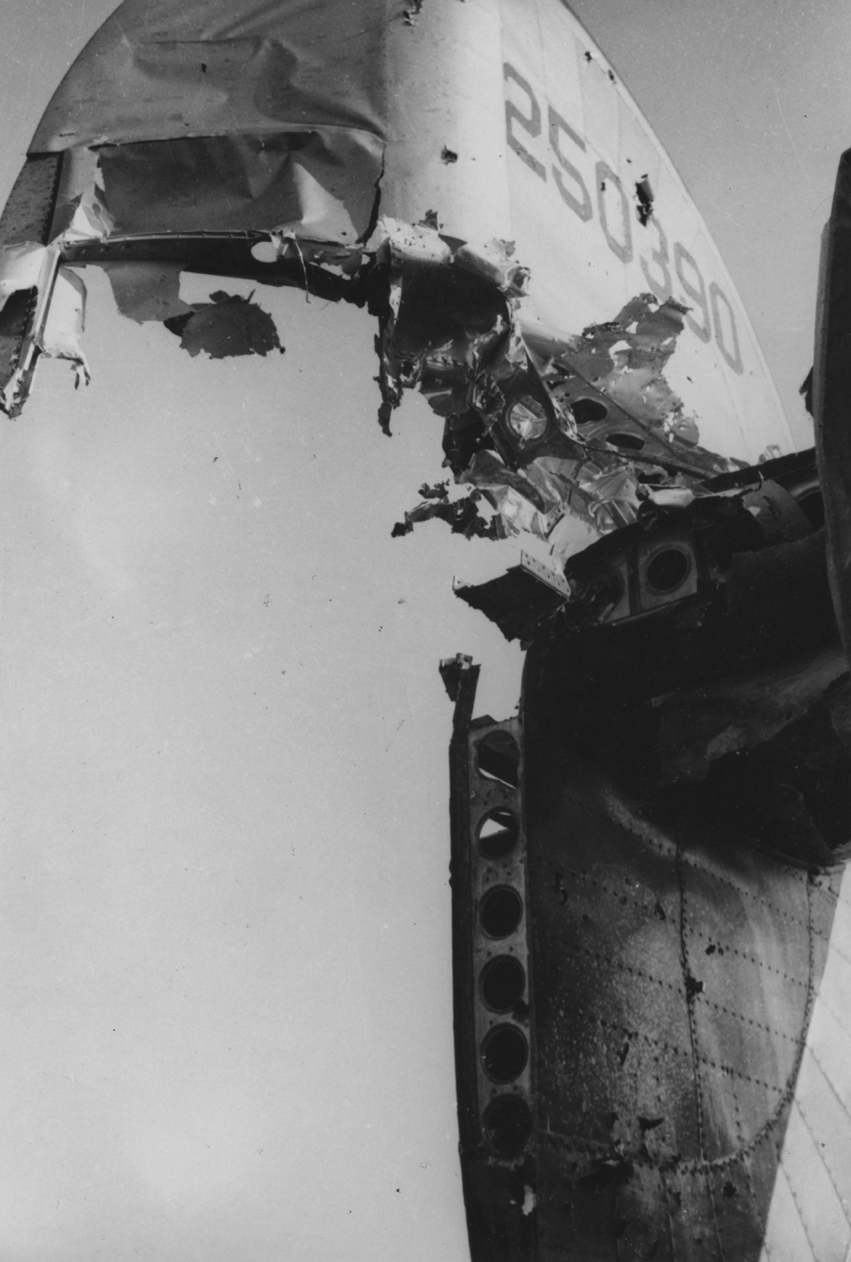 The damaged tail of a B-24 Liberator (DC-A, serial number 42-50390) of the 392nd Bomb Group. Handwritten caption on reverse: 'Battle damage - Flak? Quite a hole - eh!' Second Handwritten caption on reverse: 'Survived war, DC-A, 577BS.' Printed caption on reverse: '392BG, 577SQ.' On reverse: John E. Bode Aug 05 1964 [Stamp].