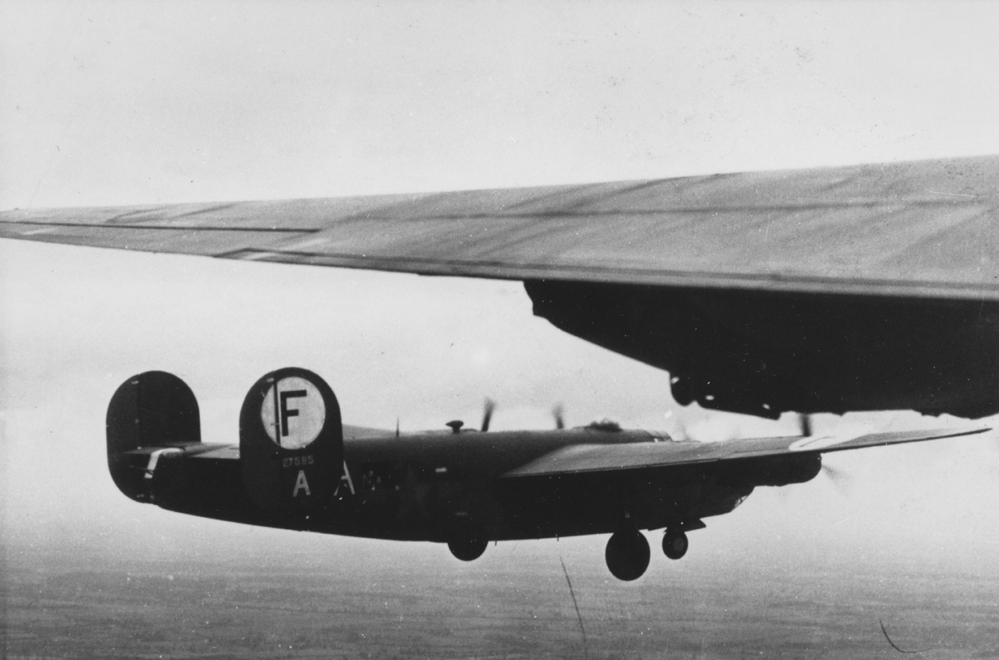 A B-24 Liberator (serial number 42-7585) of the 445th Bomb Group in flight with landing gear down. Handwritten caption on reverse: '36.'