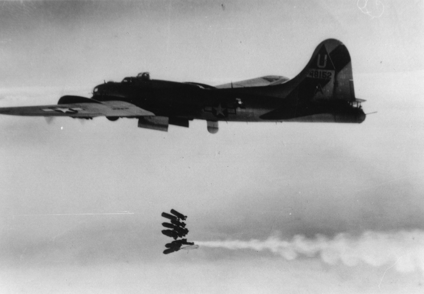 A 457th Bomb Group B-17 Flying Fortress ('A', serial number 44-8152) just after dropping its load of bombs. Another B-17 Flying Fortress is on the other side of the bomb stream, trailing smoke. Handwritten caption on reverse: '457. 93.'