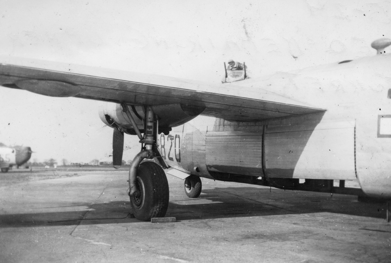 A B-24 Liberator of the 467th Bomb Group at Rackheath airfield. Its upper turret is being repaired by a crewman named "Leo". Handwritten caption on reverse: 'B-24. Leo repairing upper turret.' Second handwritten on reverse: 'C.E. Jackson, 467BG.'