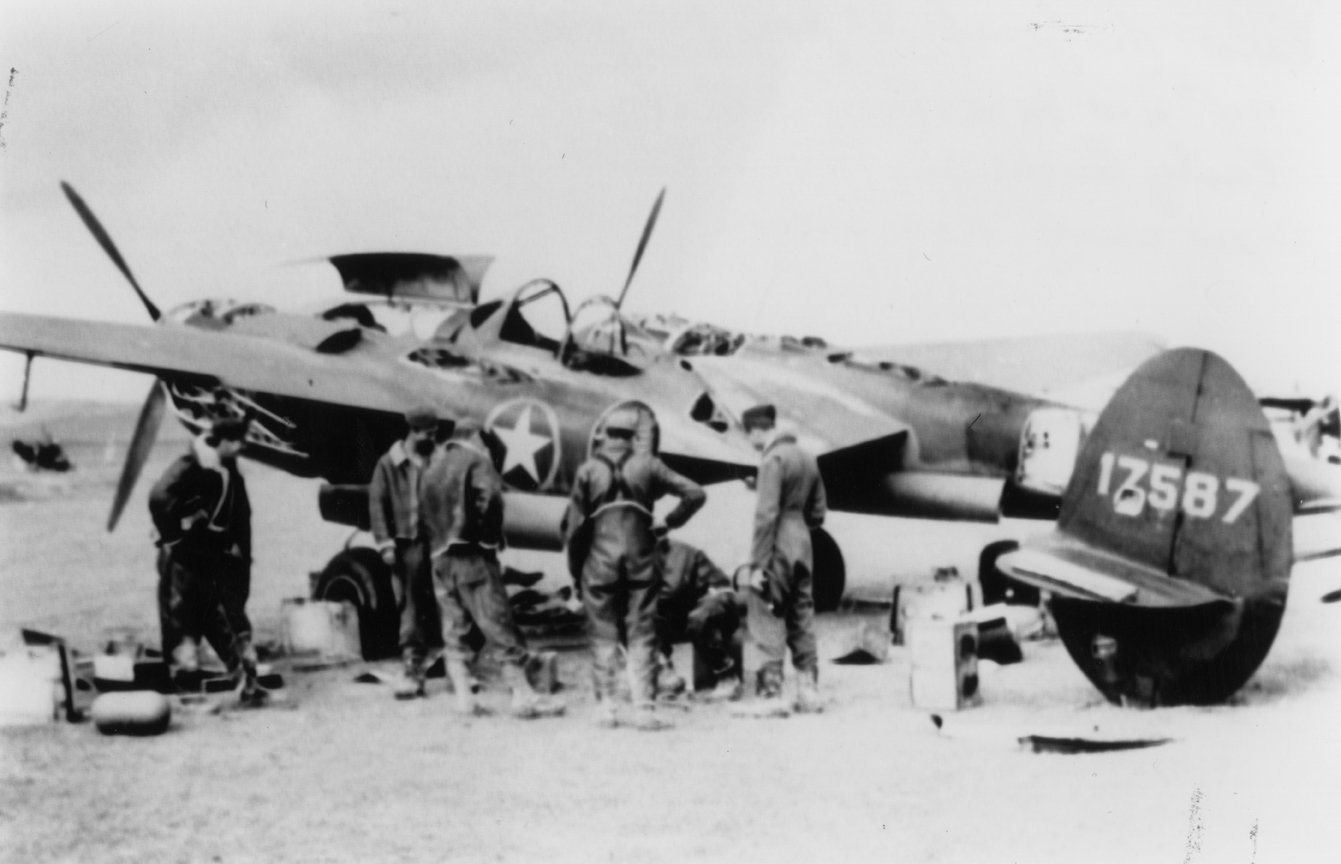 Lieutenant Jack Ilfrey (right) of the 1st Fighter Group, 15th Air Force with his P-38 Lightning (serial number 41-7587). Handwritten caption on reverse: 'P38F-1-LO 41-7587, Pilot 1/Lt Jack Ilfrey far right 94th "Hat in the Ring" 7th Sq, 1st Ftr Gp. Early Decemeber 1942- Yonks Les Bains, Algeria, No Africa. Crew Chief Roy Silvers 2nd from right.'