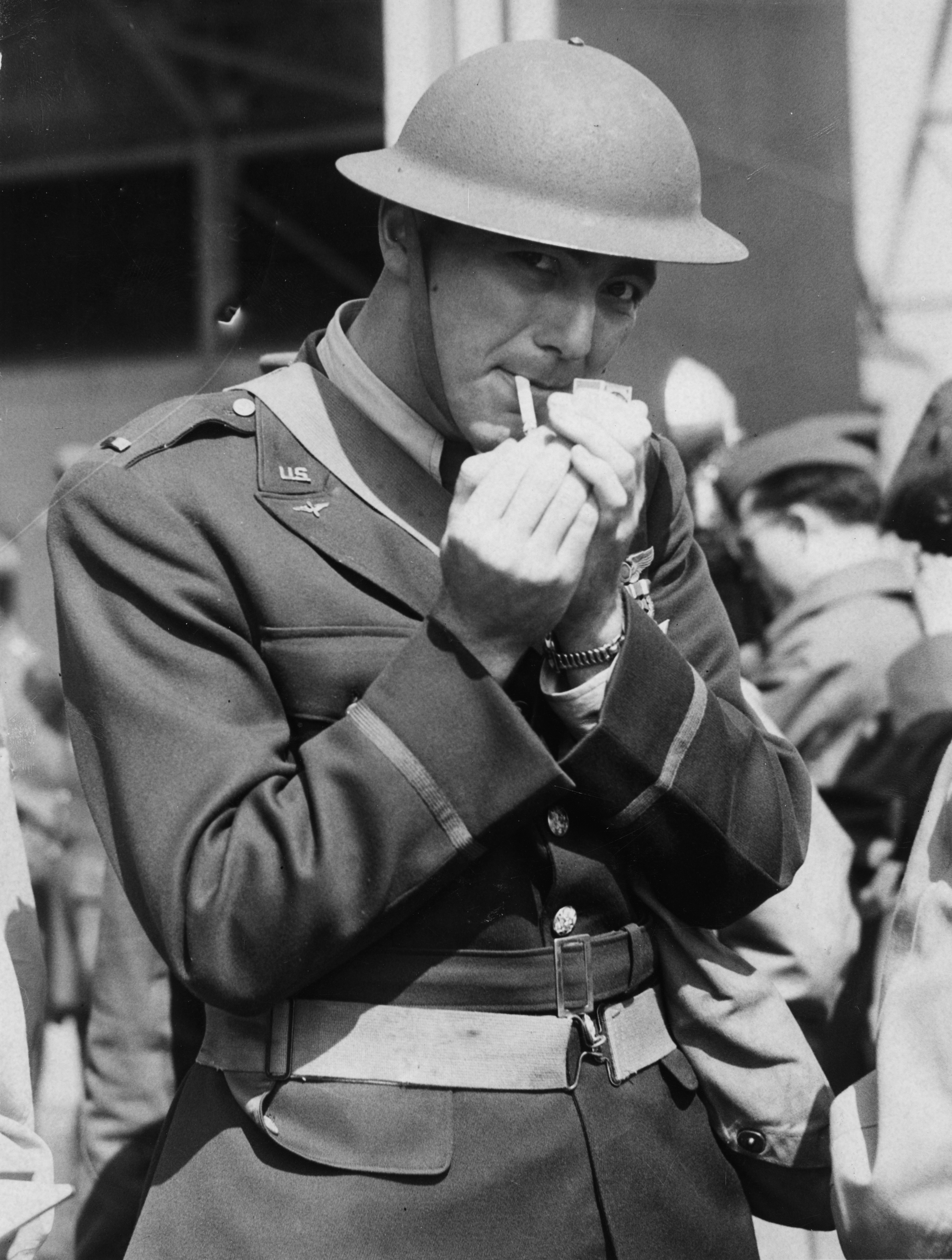 Second-Lieutenant Randall Dorton of the 301st Bomb Group smokes a cigarette after receiving the Dintinguished Flying Cross. Image stamped on reverse: 'Graphic Photo Union' [stamp] Printed caption on reverse: 'AMERICAN PILOTS DECORATED. Pilots of the American Army Air Corps, who celebrated American Independence Day (July 4th) by taking part with the RAF in a daylight bombing raid on German occupied territory in Europe, were today decorated at an aerodrome somewhere in England [censor has ammended this to r