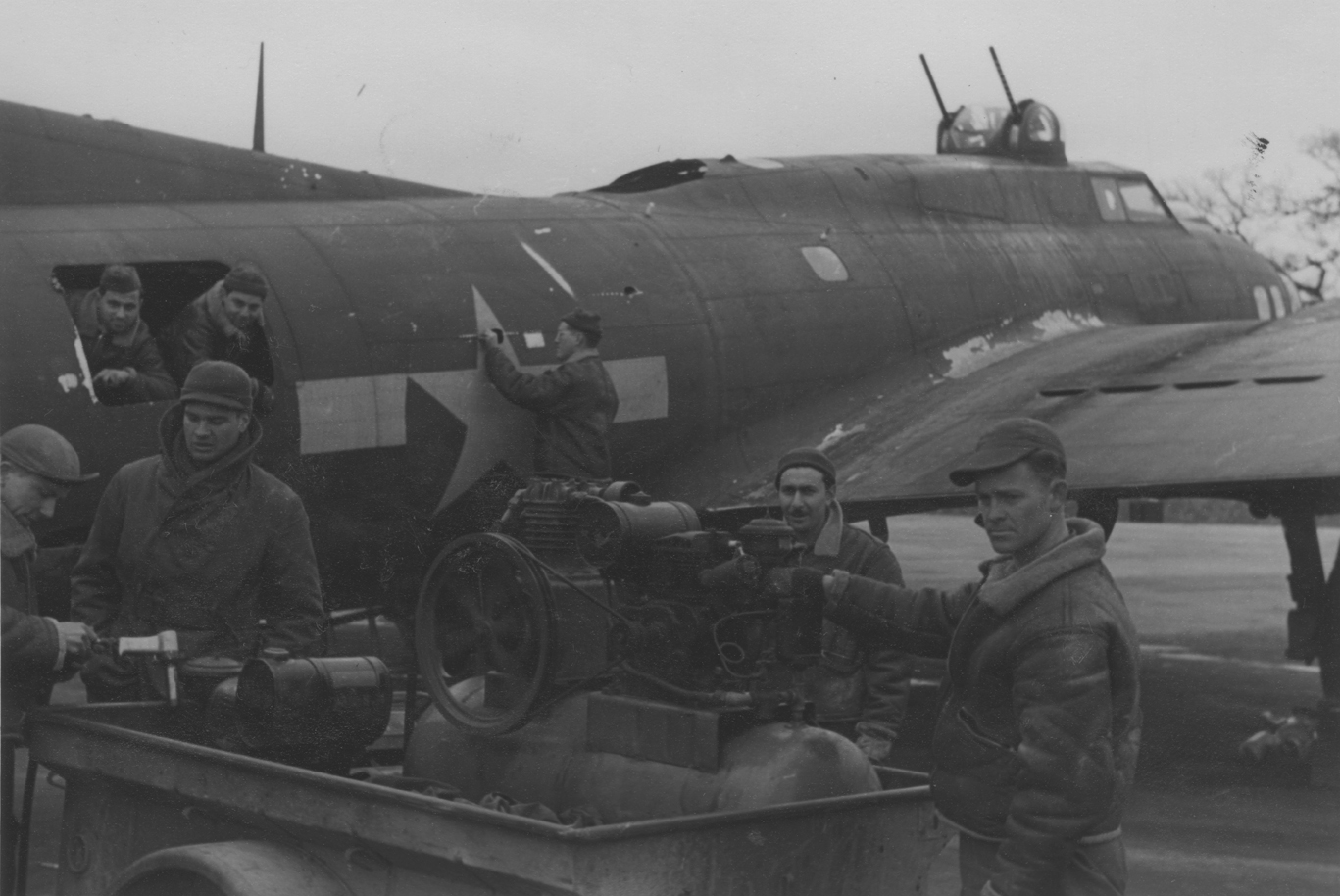 A group of fitters at work rivetting and patching over the flak holes in the fuselage of a 447th Bomb Group B-17 Flying Fortresses that had been on the 8 March 1944 Berlin raid. Passed for publication 10 Mar 1944. Printed caption on reverse: 'First Aid For Fortress Casualties. MB/Hess. Photo Shows:- Repair squad gets to work with portable rivetting gear, patching flak holes of a Fortress that was over Berlin on Wednesday's (8.3.44) raid. Fox Photos: 10th March, 1944. 21.' Censor no: 310611. On reverse: Fo