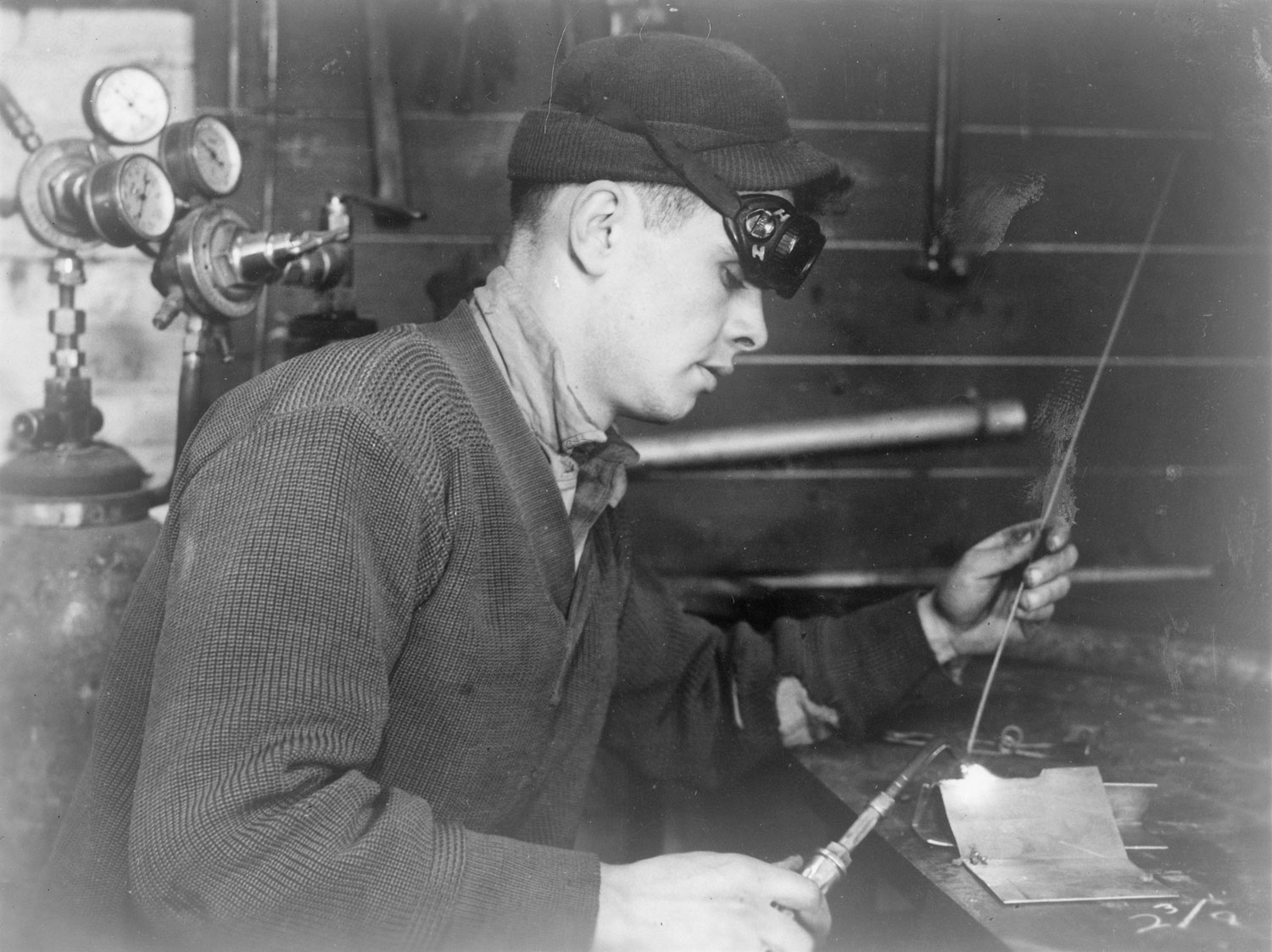 Staff Sergeant A Grundzinski  of the 78th fighter Group fashions a patch to repair bullet damage to a P-47 thunderbolt wing while working inside  the welding shop  at Duxford.  This building has now been demolished. Image from Chester Grudzinski