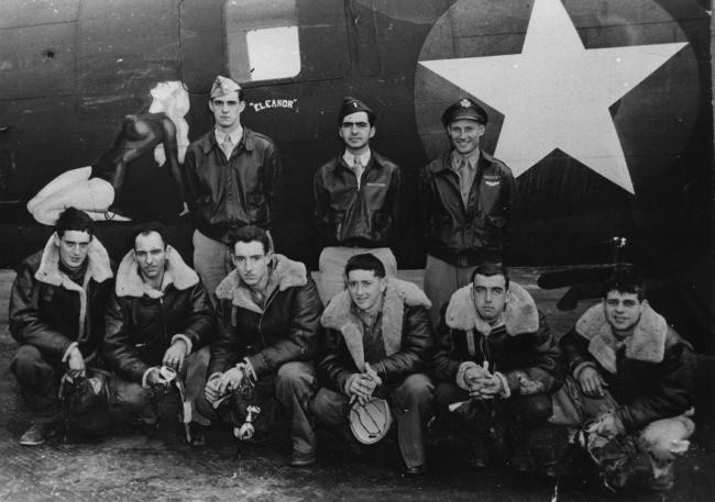 A bomber crew of the 388th Bomb Group with their B-17 Flying Fortress (serial number 42-5898) nicknamed "Little Lass". The airmen (left to right) are: Standing- Paul Williams (Pilot), Israel Rogg (Co-Pilot) and Edwin Garver (Navigator). Kneeling- Ralph Cornwall (Waist Gunner), Alfred Gardin (Radio Operator), Ray Harwood (Top Turret Gunner), Roland Conners (Tail Gunner), Maynard Rollins (Waist Gunner) and Harold Moore (Ball Turret Gunner).