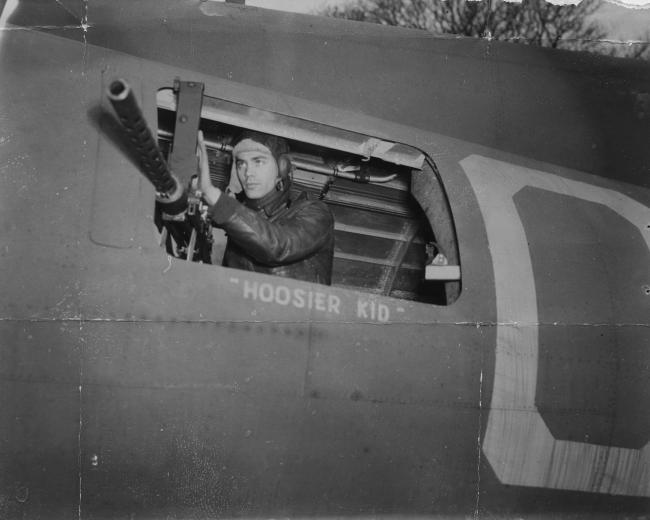 Staff Sergeant Richard C. Fortunak of the 303rd Bomb Group, checks his machine gun on his B-17 Flying Fortress. Passed for publication 25 Jan 1943. Printed caption on reverse: 'How The Boys Live And Work At Flying Fortress Station In England. Wide World Photo Shows:- Staff Sgt. Richard C. Fortunak, 1260 West 17th Avenue, Gary, Ind., Waist Gunner in a Fortress, which he and his crew mates have named "Hoosier Kid", adjusts gun in his turret. WW/ALA. 26-1-43.' On reverse: Associated Press, US Army Press Cens